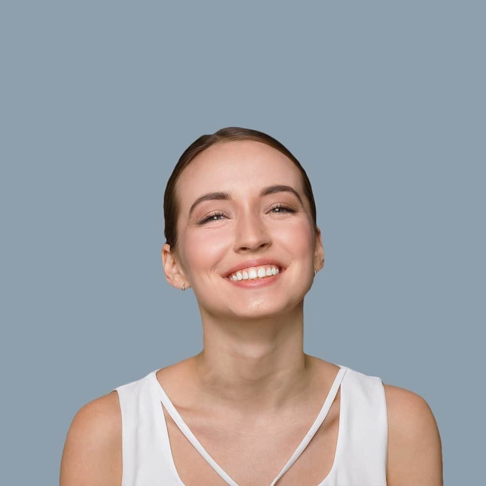 Young woman with radiant skin smiling against a plain background, emphasizing beauty and health.